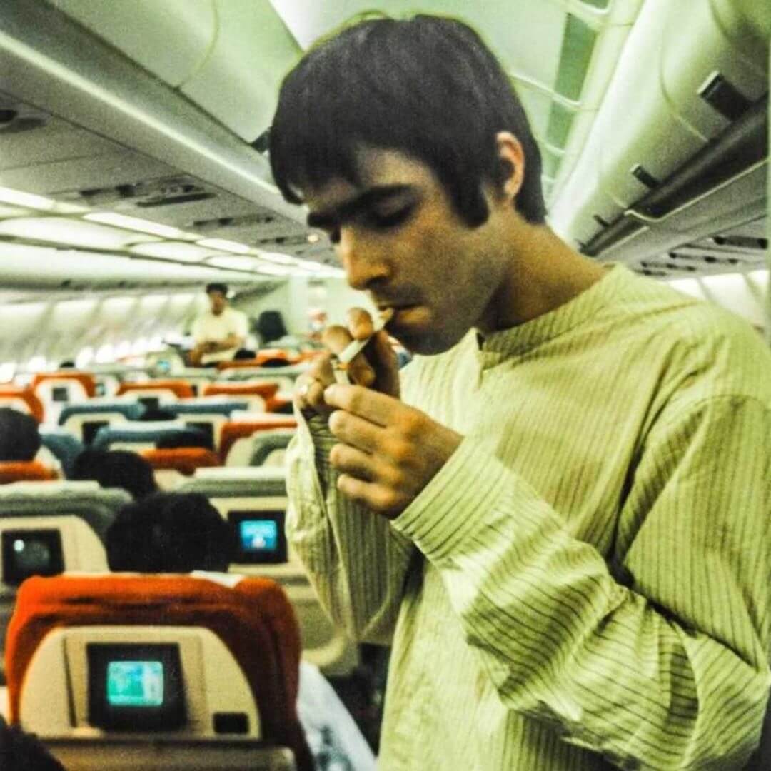 Liam lighting a cigarette fronm another cigarette on a plane